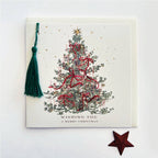 A square Christmas greeting card with a white textured background, featuring an illustrated decorated Christmas tree with red ribbons and a gold star. A dark green tassel hangs from the top-left corner, and the text 'WISHING YOU A MERRY CHRISTMAS' is printed at the bottom.