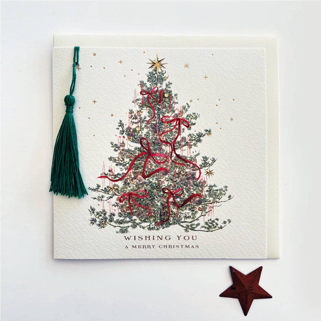 A square Christmas greeting card with a white textured background, featuring an illustrated decorated Christmas tree with red ribbons and a gold star. A dark green tassel hangs from the top-left corner, and the text 'WISHING YOU A MERRY CHRISTMAS' is printed at the bottom.