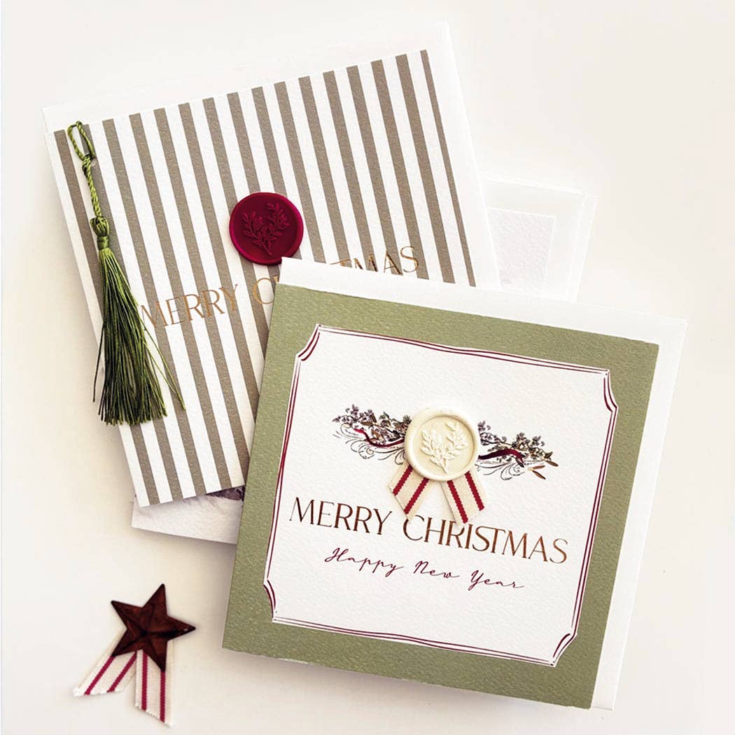 A festive greeting card set arranged on a light cream background. The main card in front is white with an olive green border and reads 'MERRY CHRISTMAS Happy New Year' under a cream wax seal motif.